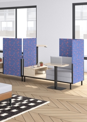 Espace de travail individuel avec sofa gris et s&eacute;parateurs bleus. Cet espace est plac&eacute; dans un espace lumineux avec des planchers en bois &agrave; motif de chevrons