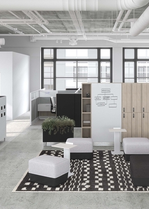 Grand espaces de bureaux ouverts, avec cubicules en bois gris&eacute; clair. L'espace central comporte un tapis, un tableau blanc, un espace de r&eacute;union