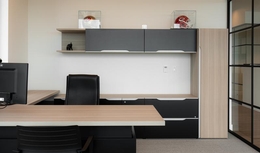 Bureau fermé avec bureau en coin avec un fini en bois. Chaise noire et étagères charcoal. Mur vitré et accessoires modernes