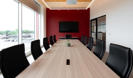 Grande salle de réunion avec mur rouge, chaises ergonomiques noires et table avec fini en bois clair.