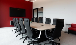 Grande salle de réunion avec mur rouge, chaises ergonomiques noires et table avec fini en bois clair.