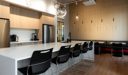 Espace cuisine moderne et avec finis en bois clair. Ilôt en céramique blanc avec chaises hautes noires modernes. Lampes de plafond modernes.