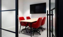 Salle de réunion fermée avec murs vitrés. Chaises sur roulettes confortables rouges avec table avec fini en bois clair.